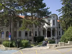 Историческата сграда на Учредителното събрание във Велико Търново с бяла фасада, керемиден покрив и високи борове отпред