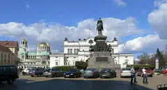 Сградата на Народното събрание в София с паметника на Цар Освободител, катедралата „Св. Александър Невски“ и паркирани коли на площада